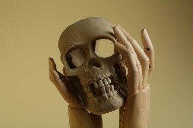 Photo of Wooden mannequin hands holding human skull on beige background