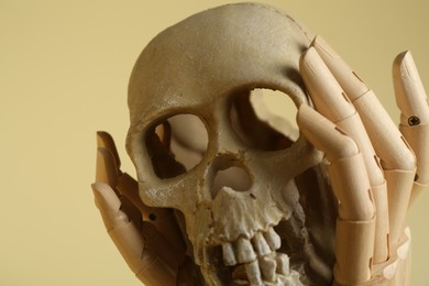 Wooden mannequin hands holding human skull on beige background, closeup