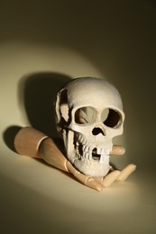 Photo of Wooden mannequin hand holding human skull on beige background