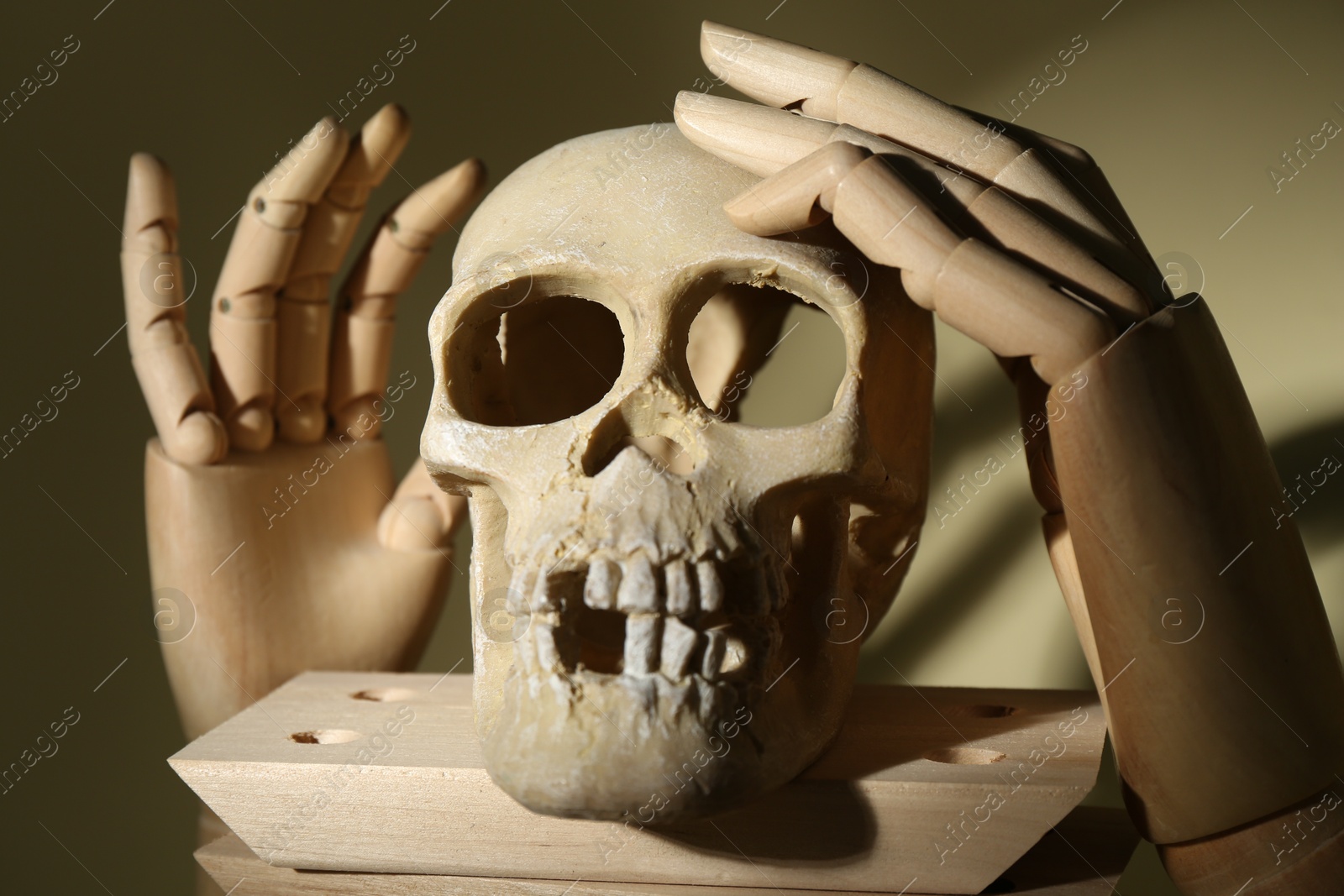 Photo of Human skeleton made of skull, wooden blocks and mannequin hands on beige background, closeup