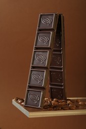 Photo of Pieces of tasty chocolate bar and coffee beans on glass surface against brown background