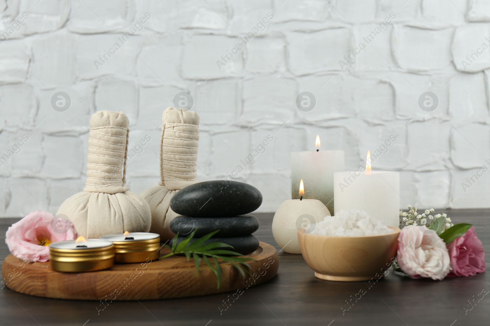 Photo of Massage bags, spa stones, sea salt, burning candles and flowers on wooden table