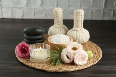 Massage bags, spa stones, sea salt, burning candle and flowers on wooden table