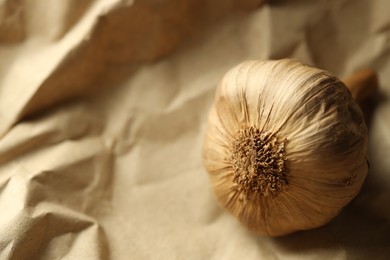 Bulb of raw garlic on crumpled beige paper, closeup. Space for text