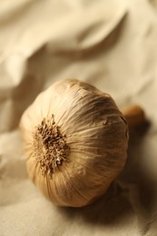 Bulb of raw garlic on crumpled beige paper, closeup