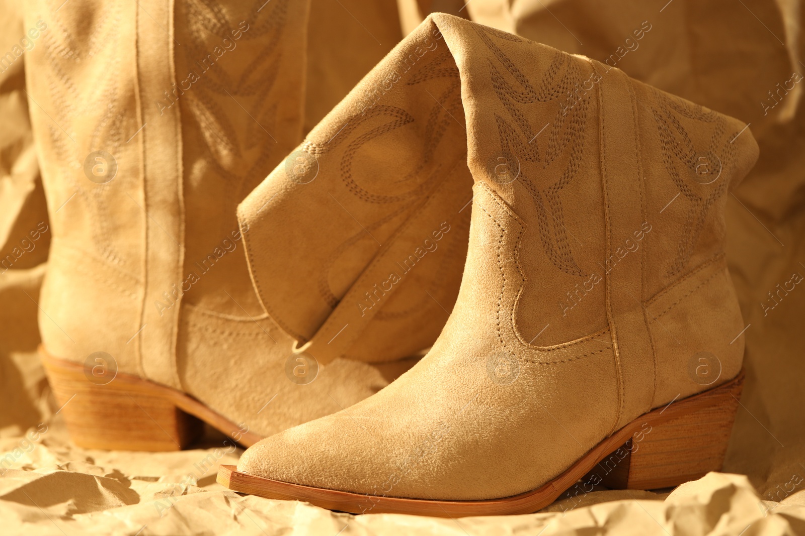 Photo of Pair of stylish boots on crumpled beige paper, closeup