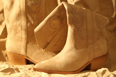 Photo of Pair of stylish boots on crumpled beige paper, closeup