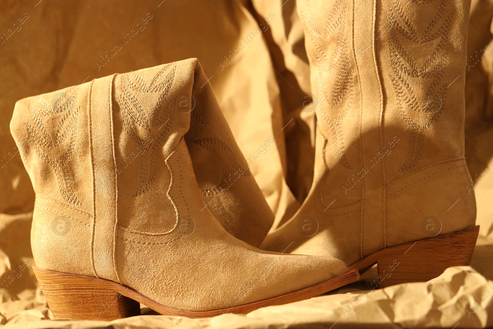 Photo of Pair of stylish boots on crumpled beige paper, closeup