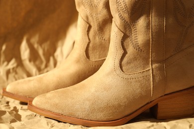 Photo of Pair of stylish boots on crumpled beige paper, closeup