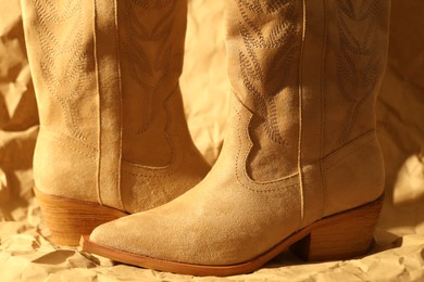 Photo of Pair of stylish boots on crumpled beige paper, closeup