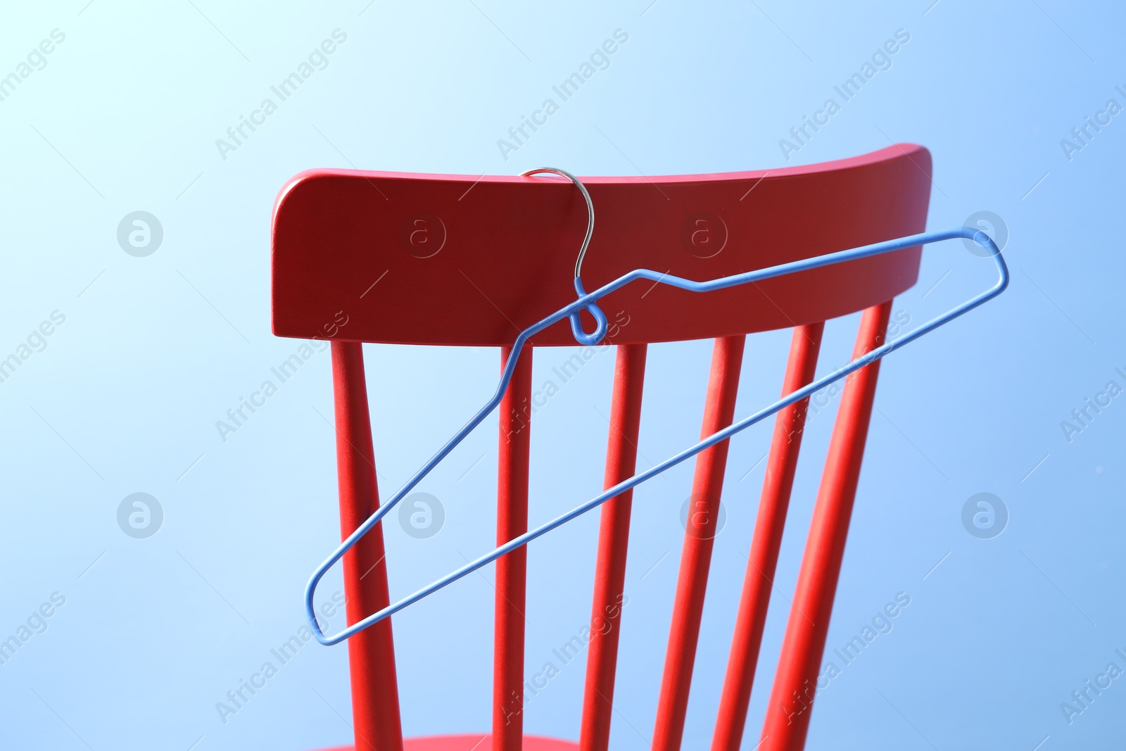 Photo of Red wooden chair and clothing hanger on light blue background, closeup