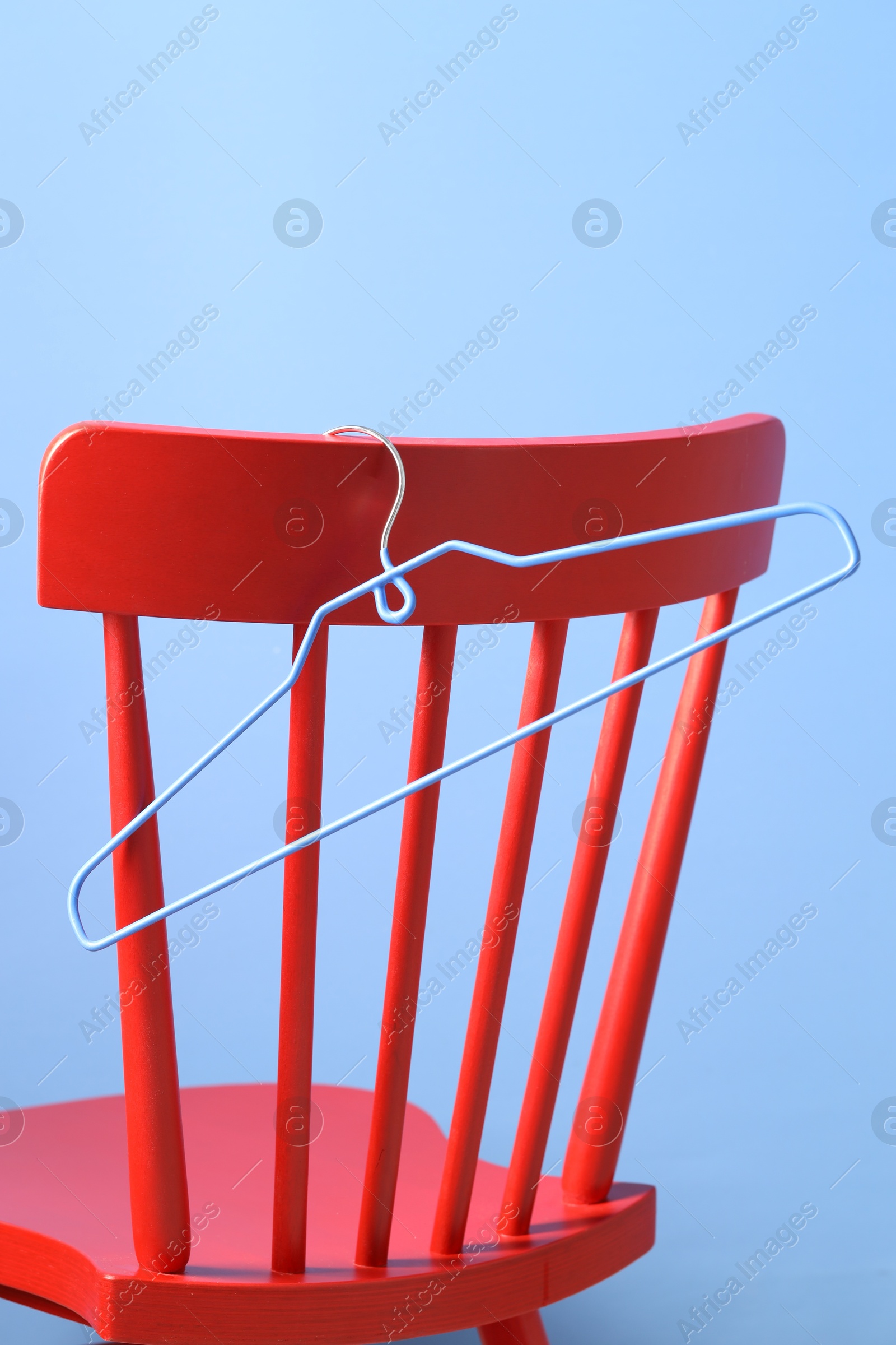 Photo of Red wooden chair and clothing hanger on light blue background, closeup