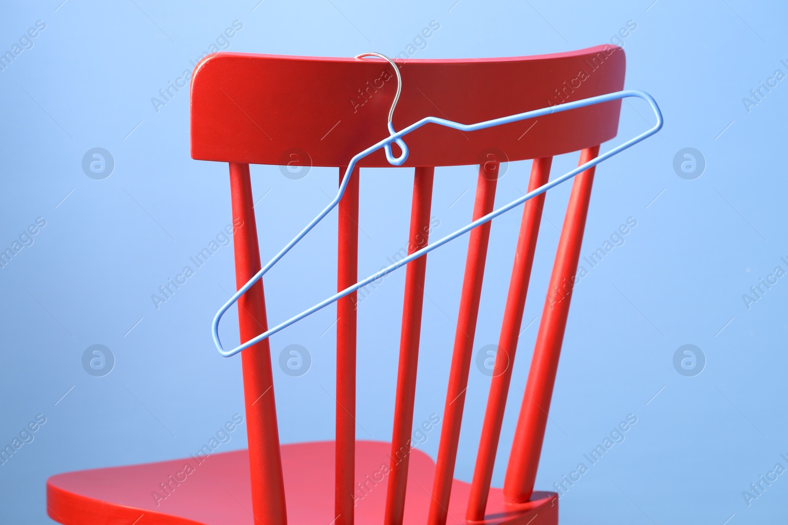 Photo of Red wooden chair and clothing hanger on light blue background, closeup