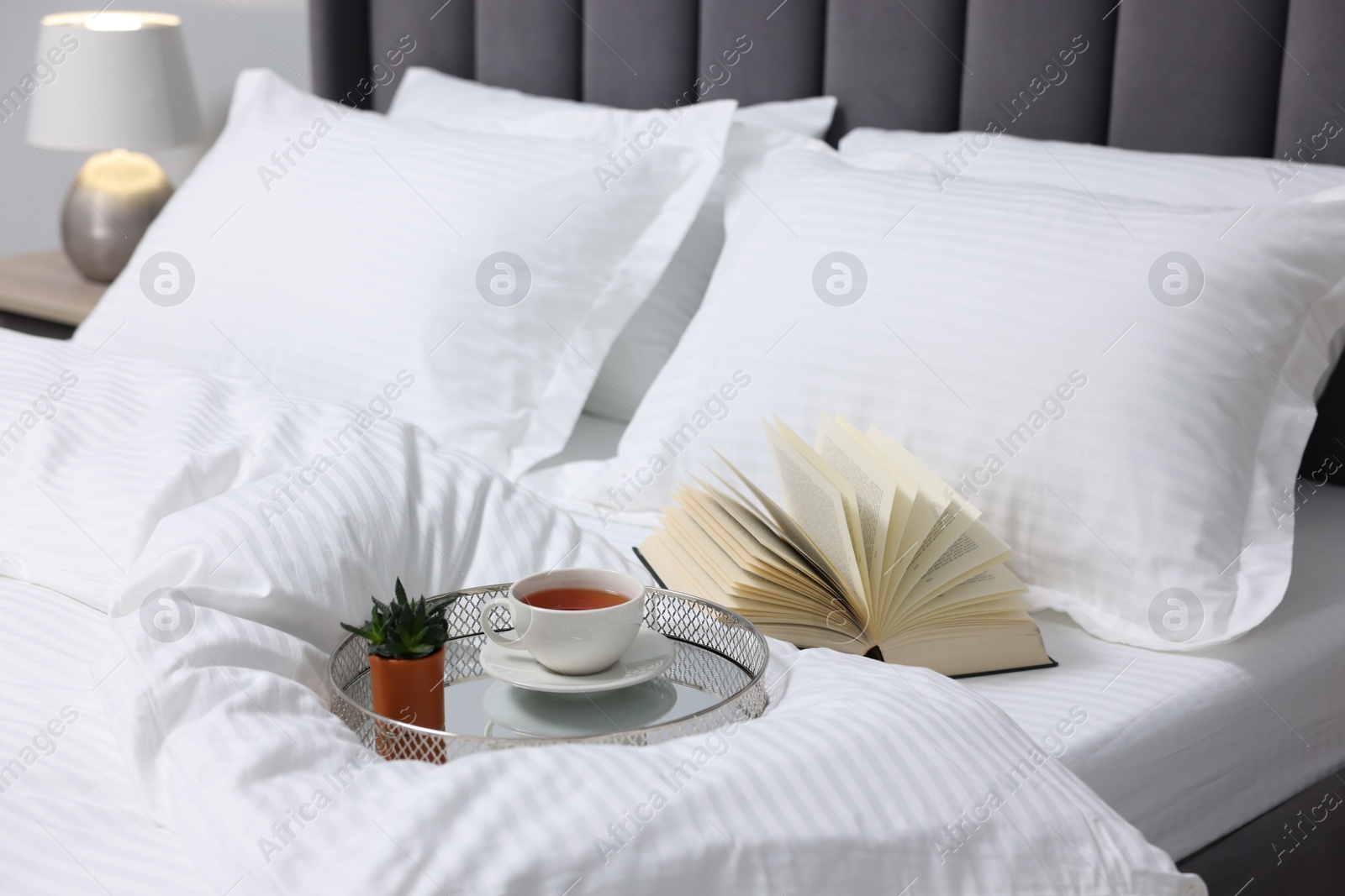 Photo of Tea, book and floral decor on bed with clean linens indoors