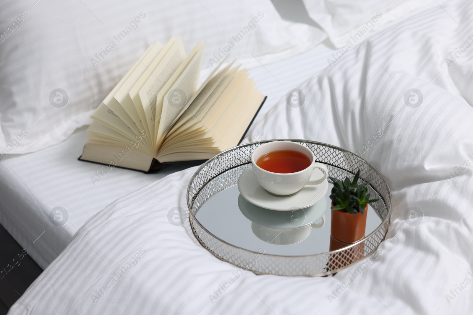 Photo of Tea, book and floral decor on bed with clean linens indoors