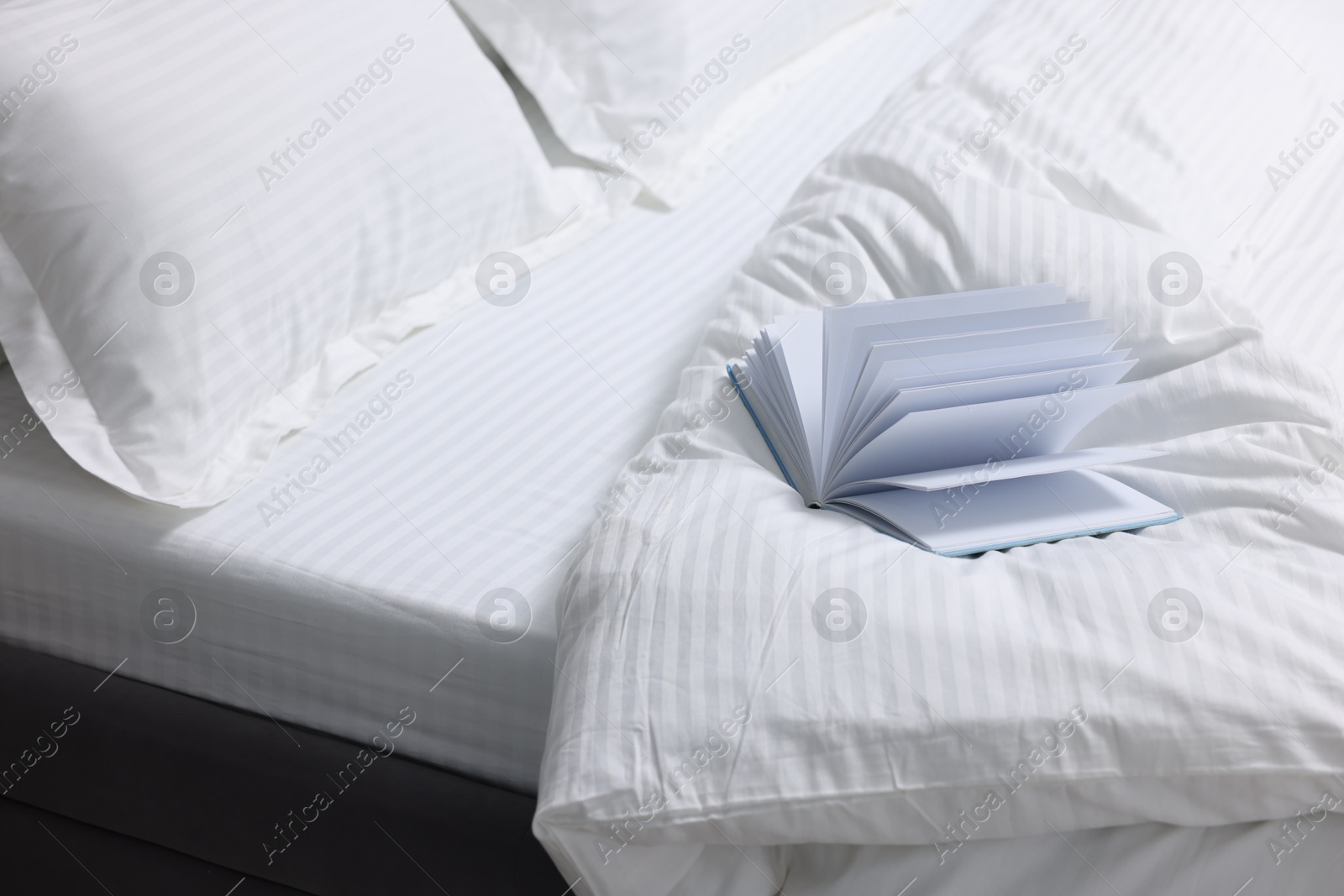 Photo of Open book on bed with clean linens indoors