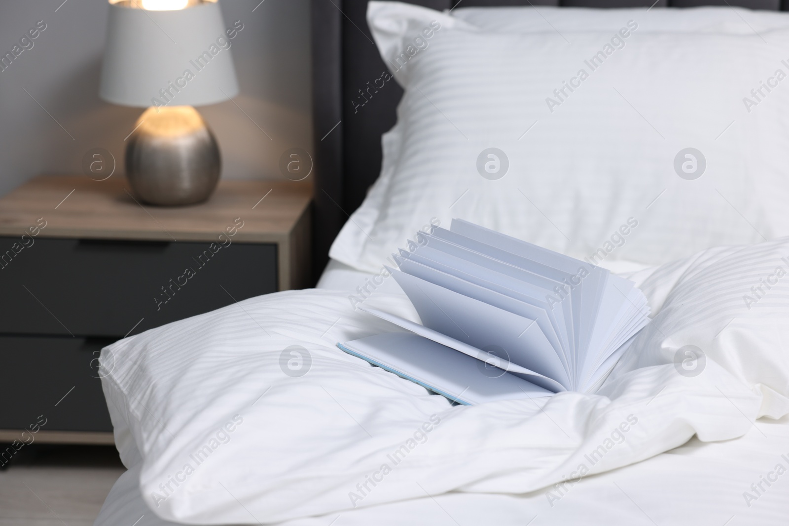 Photo of Open book on bed with clean linens indoors