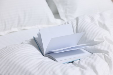 Photo of Open book on bed with clean linens indoors