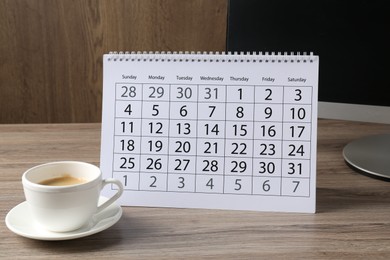 Photo of Timetable. Monthly planner, coffee and computer on wooden table