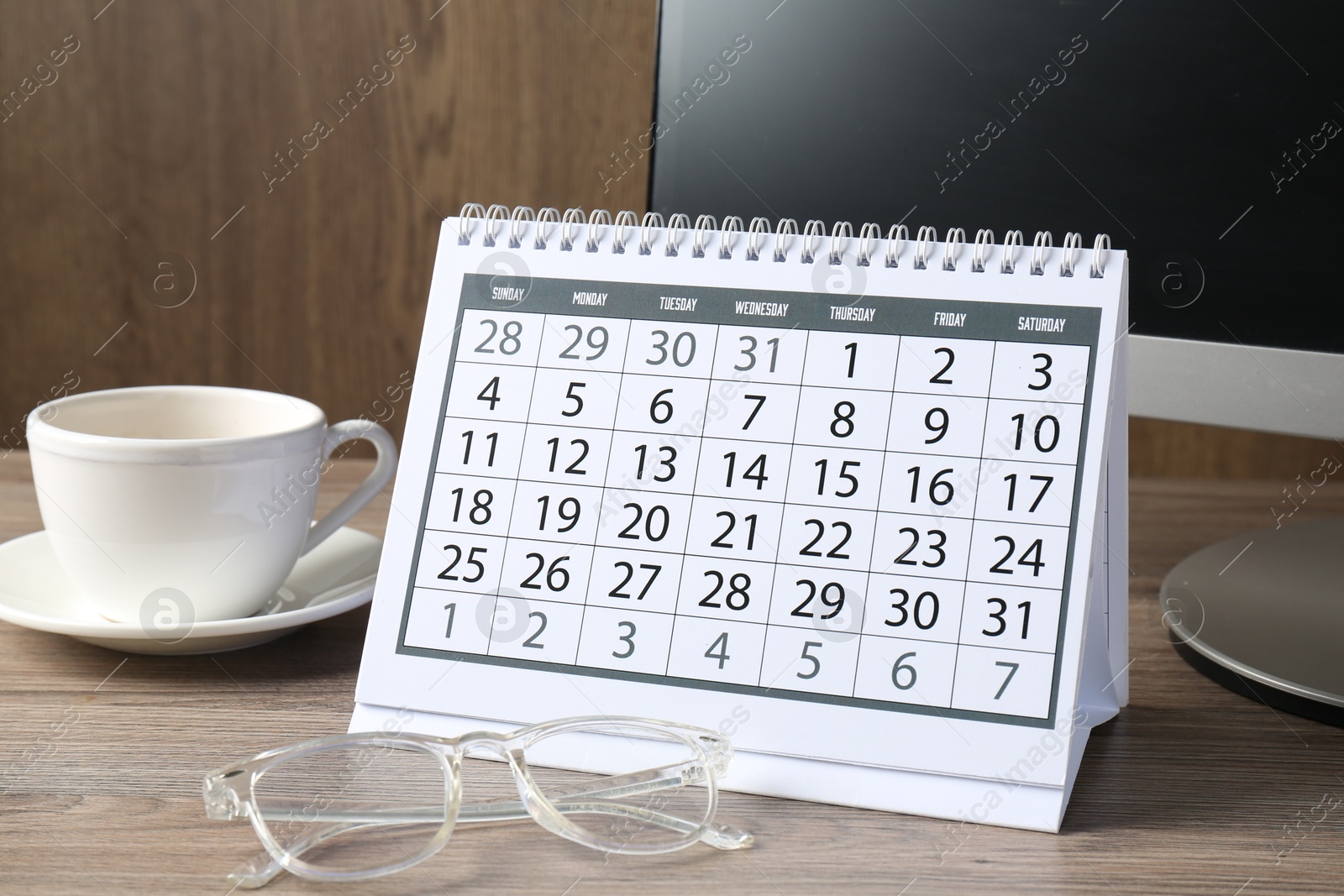 Photo of Timetable. Monthly planner, glasses, coffee and computer on wooden table