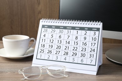 Photo of Timetable. Monthly planner, glasses, coffee and computer on wooden table