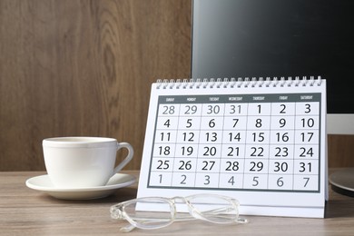 Photo of Timetable. Monthly planner, glasses, coffee and computer on wooden table