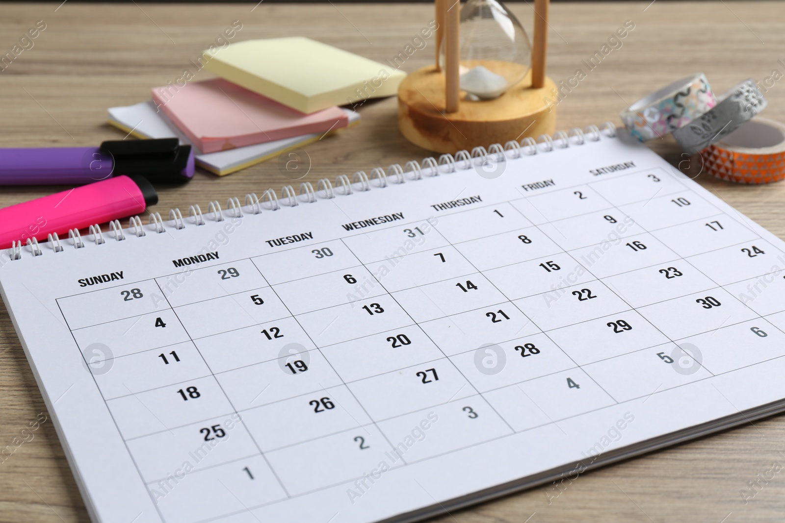 Photo of Timetable. Monthly planner and stationery on wooden table, closeup