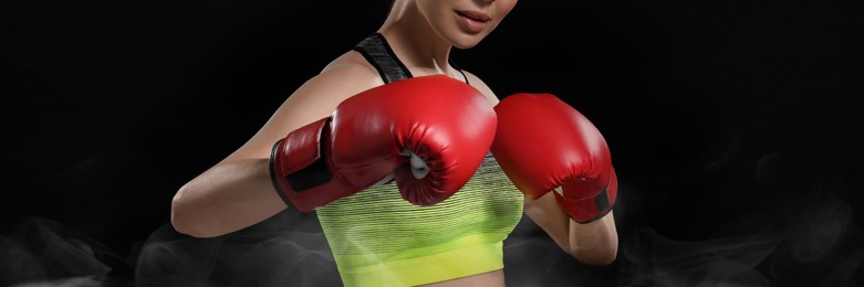 Image of Woman in boxing gloves training on black background, closeup. Banner design