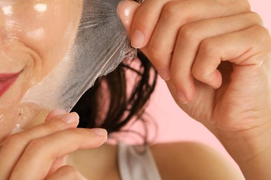 Photo of Woman peeling off face mask on pink background, closeup