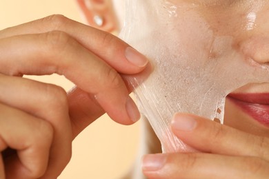 Woman peeling off face mask on beige background, closeup