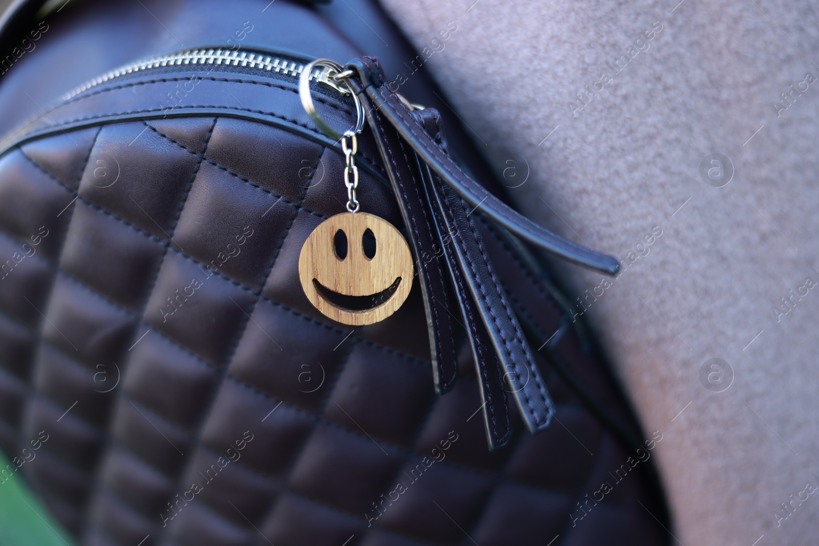 Photo of Backpack with wooden keychain in shape of smiley face and black leather decor, closeup. Selective focus