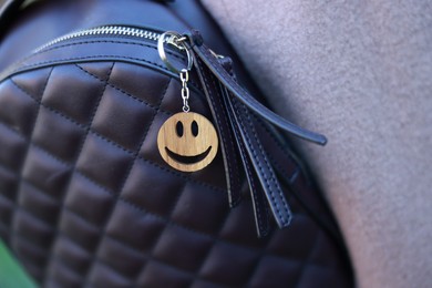 Photo of Backpack with wooden keychain in shape of smiley face and black leather decor, closeup. Selective focus