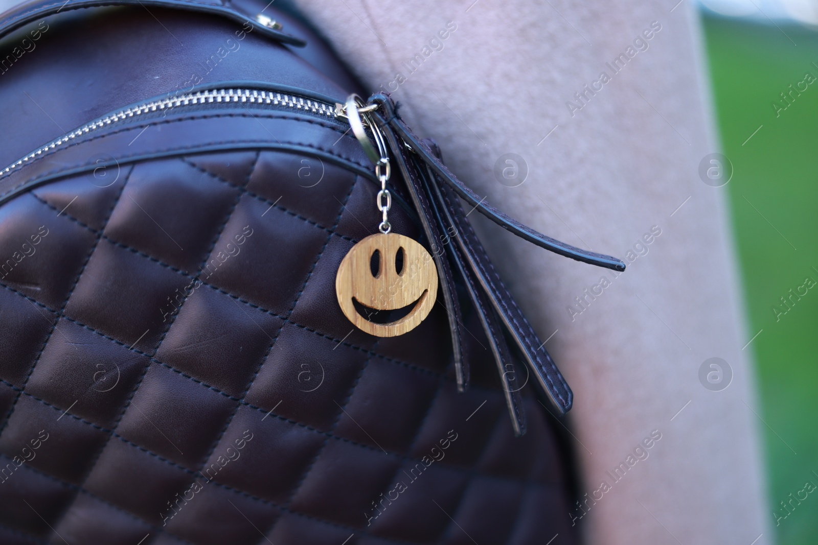 Photo of Backpack with wooden keychain in shape of smiley face and black leather decor, closeup. Selective focus