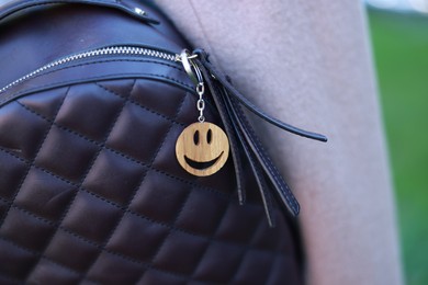 Photo of Backpack with wooden keychain in shape of smiley face and black leather decor, closeup. Selective focus