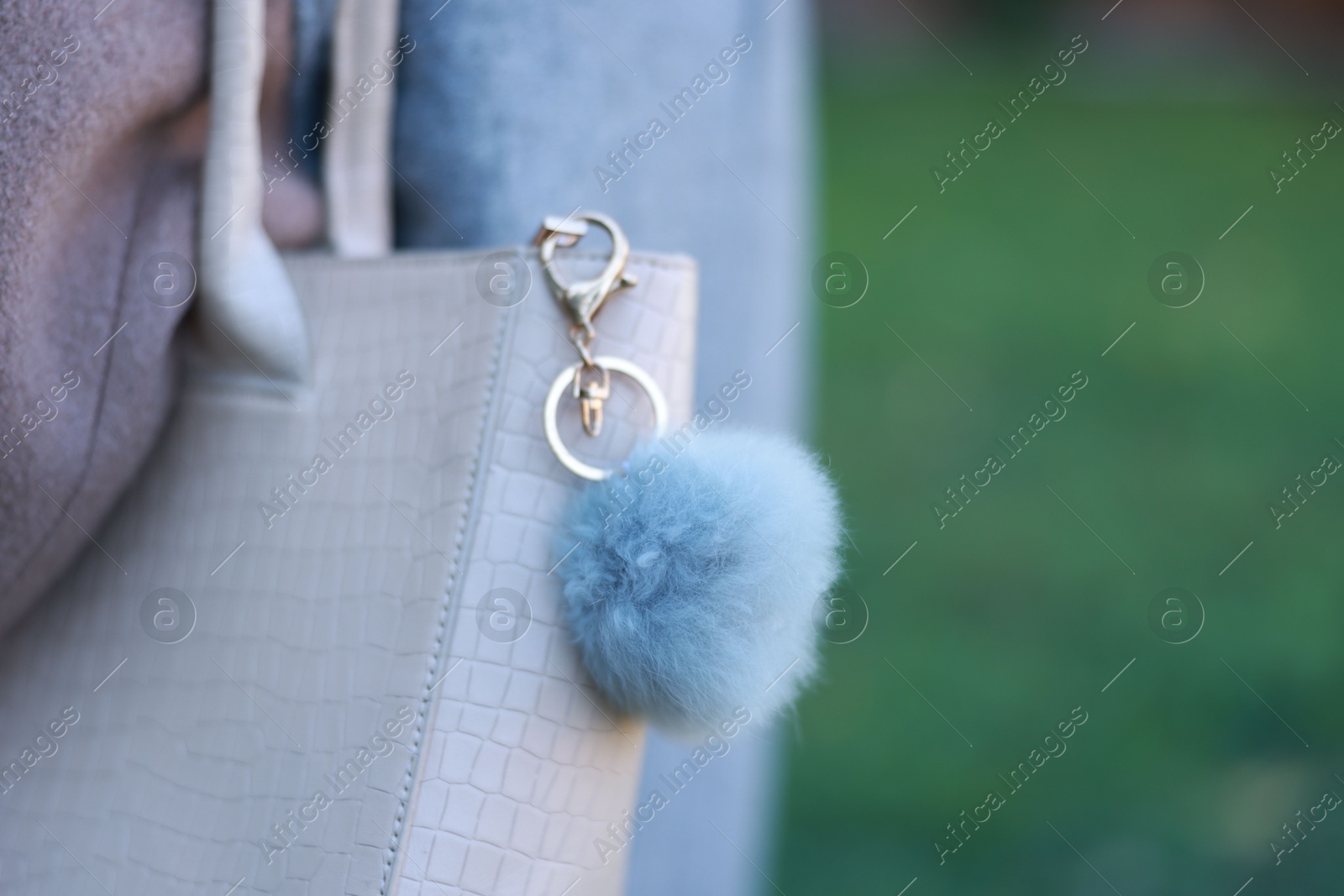 Photo of Woman with faux fur keychain on her bag outdoors, closeup. Selective focus