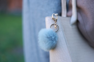 Photo of Woman with faux fur keychain on her bag outdoors, closeup. Selective focus