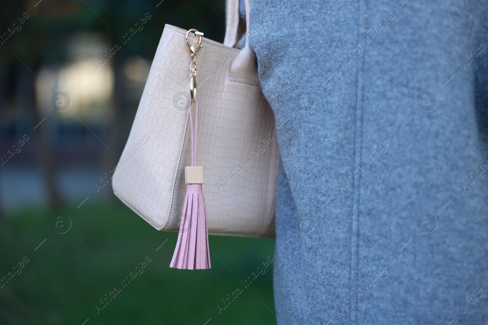 Photo of Woman with pink leather keychain on her bag outdoors, closeup