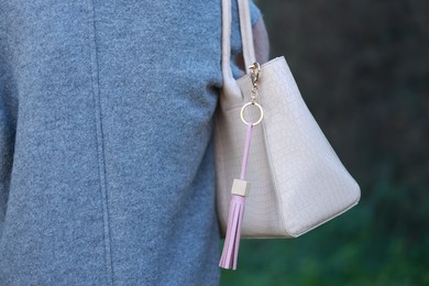 Photo of Woman with pink leather keychain on her bag outdoors, closeup