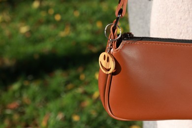 Photo of Stylish bag with wooden keychain in shape of smiley face outdoors, closeup. Space for text