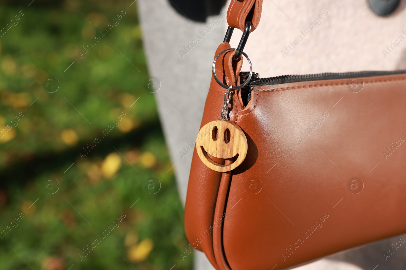 Photo of Stylish bag with wooden keychain in shape of smiley face outdoors, closeup. Space for text