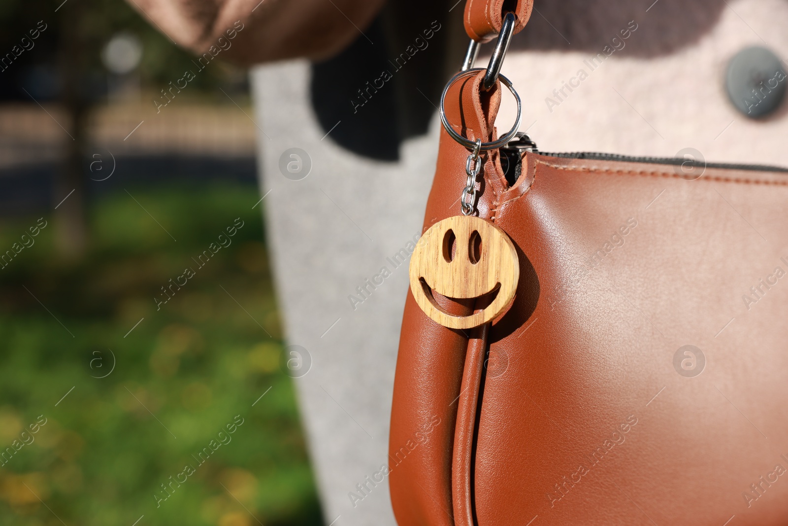 Photo of Woman with wooden keychain in shape of smiley face on her bag outdoors, closeup