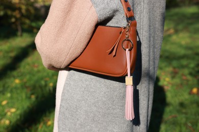 Photo of Woman with pink leather keychain on her bag outdoors, closeup