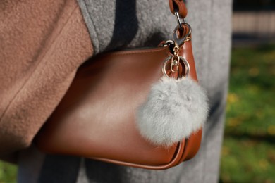 Photo of Woman with faux fur keychain on her bag outdoors, closeup