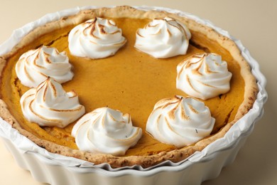 Tasty homemade pumpkin pie in baking dish on beige table, closeup