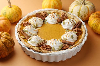 Delicious homemade pumpkin pie in baking dish and fresh pumpkins on orange table, closeup