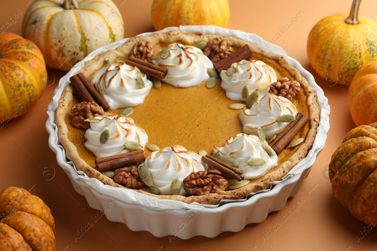 Photo of Delicious homemade pumpkin pie in baking dish and fresh pumpkins on orange table, closeup