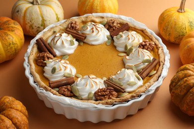 Delicious homemade pumpkin pie in baking dish and fresh pumpkins on orange table, closeup