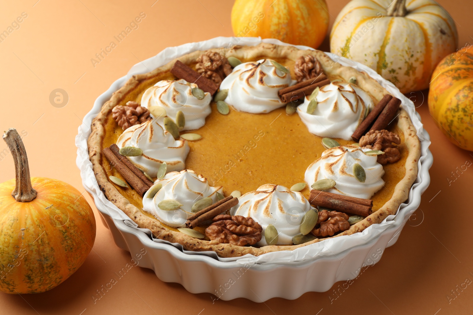 Photo of Delicious homemade pumpkin pie in baking dish and fresh pumpkins on orange table, closeup