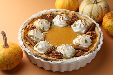 Delicious homemade pumpkin pie in baking dish and fresh pumpkins on orange table, closeup