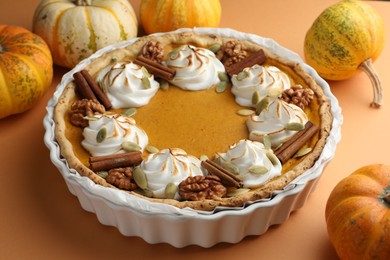 Delicious homemade pumpkin pie in baking dish and fresh pumpkins on orange table, closeup